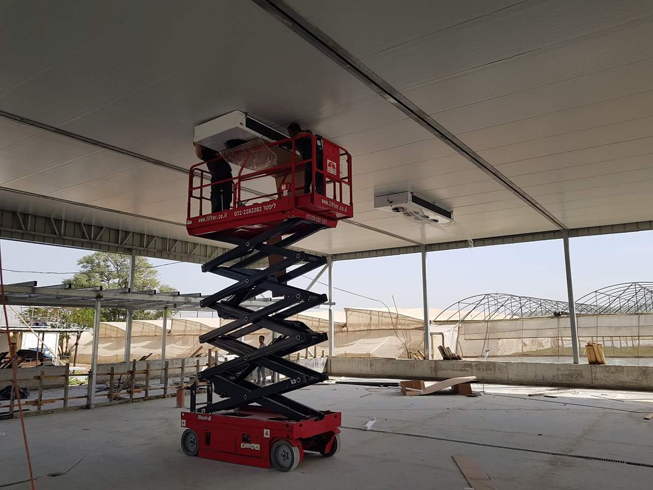 במת הרמה אדומה נושאת שני אנשי צוות שמתקינים מזגן תקרה גדול בתוך מבנה גדול.
